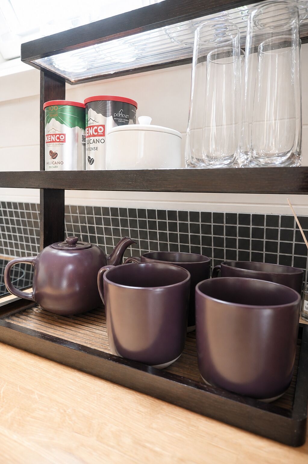 Una repisa de cocina con una tetera, tazas y recipientes para café.