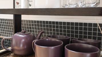 Una repisa de cocina con una tetera, tazas y recipientes para café.