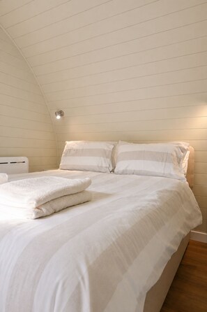 Quarto com uma cama de solteiro, roupa de cama branca e luminária no teto.