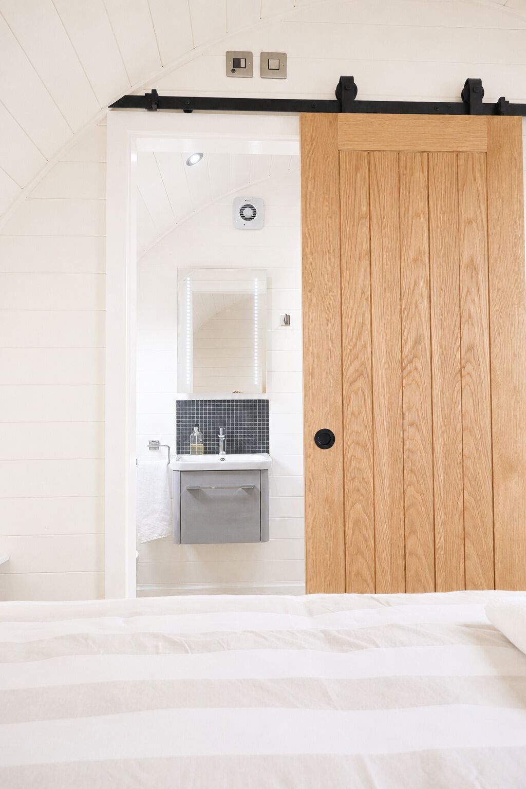 A bedroom with a bed, a wooden door, a bathroom with a mirror, and a sink.