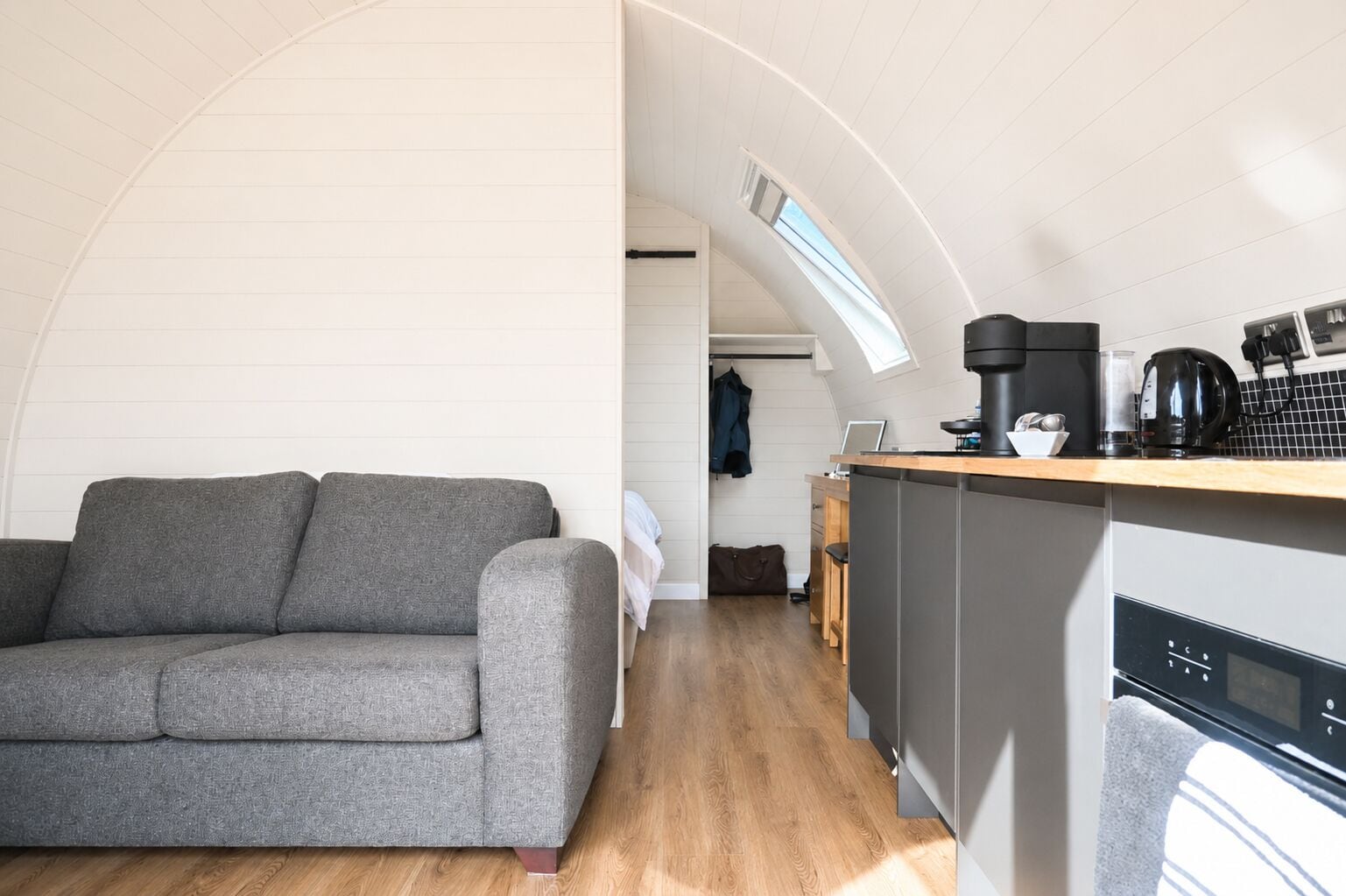 Un espace de vie compact comprenant un canapé, une kitchenette et une vue à travers une fenêtre en arc de cercle.