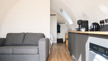 Um espaço de estar compacto com sofá, cozinha compacta e vista através de uma janela em arco.