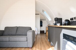 Un espacio habitable compacto con sofá, kitchenette y vistas a través de un ventanal arqueado.