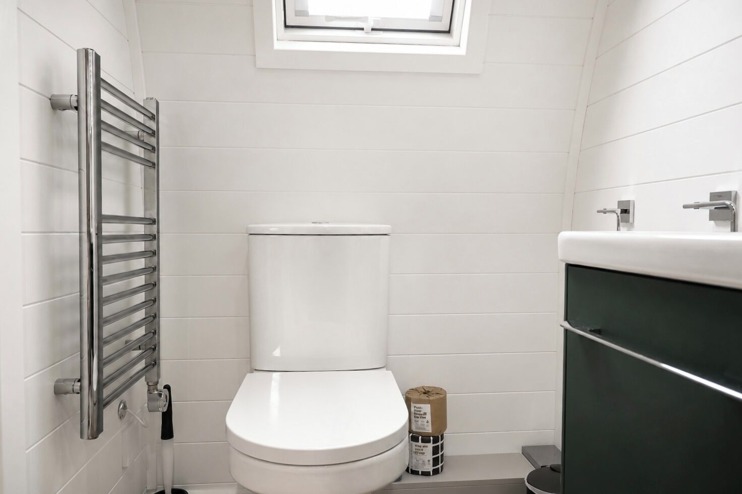 A bathroom with a white toilet, a towel rack, and a window above the toilet.