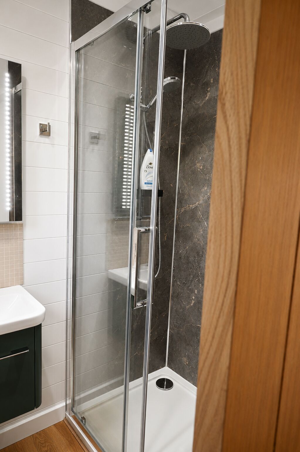 A glass-enclosed shower with a handheld showerhead and a wall-mounted faucet.