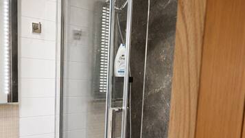 A glass-enclosed shower with a handheld showerhead and a wall-mounted faucet.