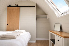 A bedroom with a bed, a wooden wardrobe, a desk with a chair, and a skylight. - Croft 21 Glamping (Beauly)