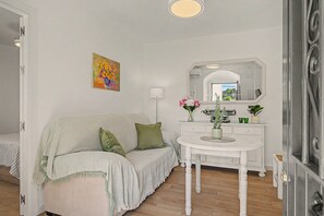 Um quarto com um sofá branco, uma mesa pequena com um vaso, um espelho e um quadro na parede.