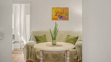 A living room with a sofa, a round table with a plant, and a painting on the wall.