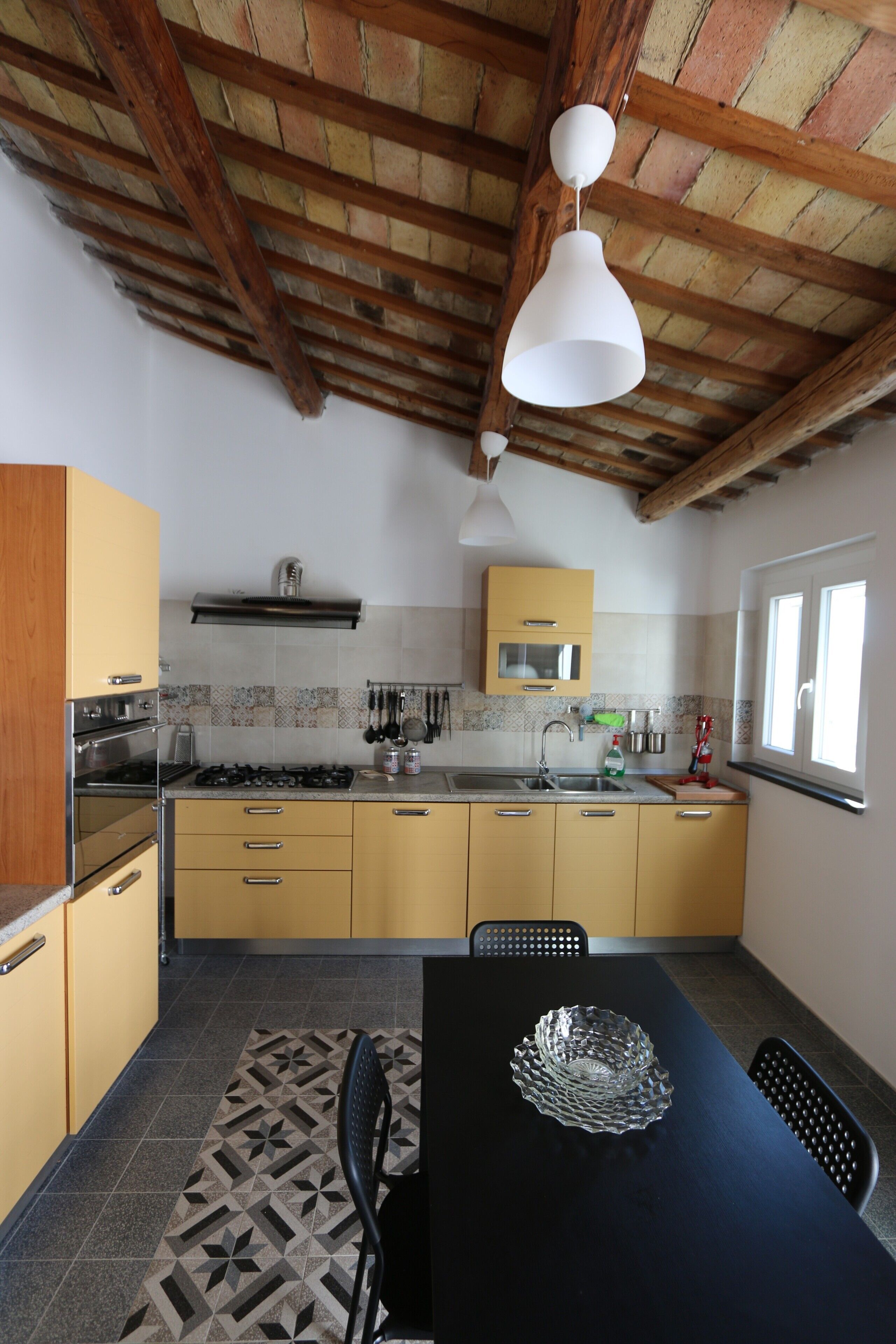Une cuisine avec des poutres en bois, une cuisinière à gaz, un évier et une table à manger avec des chaises.