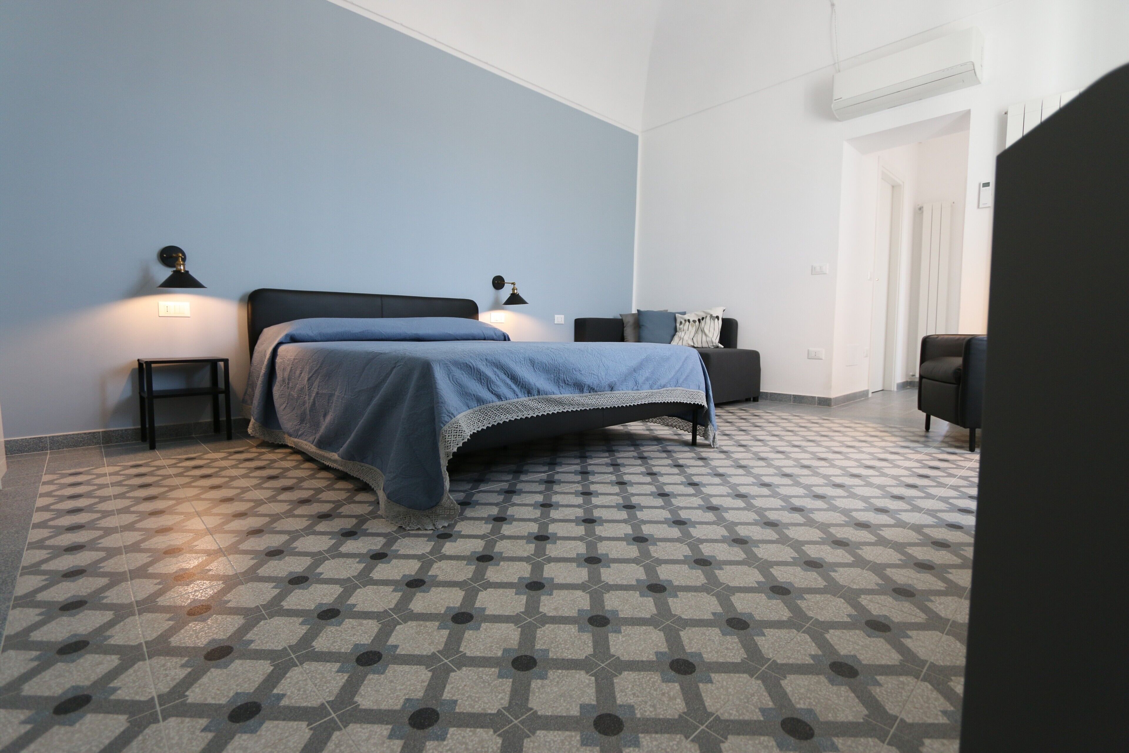 A bedroom with a bed, bedside tables, a chair, and a patterned floor.