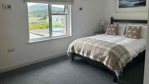 A bedroom with a bed, a window with a view, and a painting on the wall.