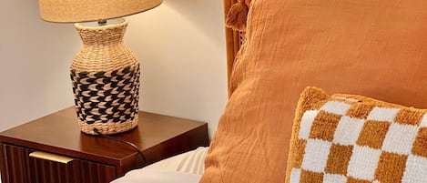 A bed with a checkered pillow, a lamp on a bedside table, and a textured wall.