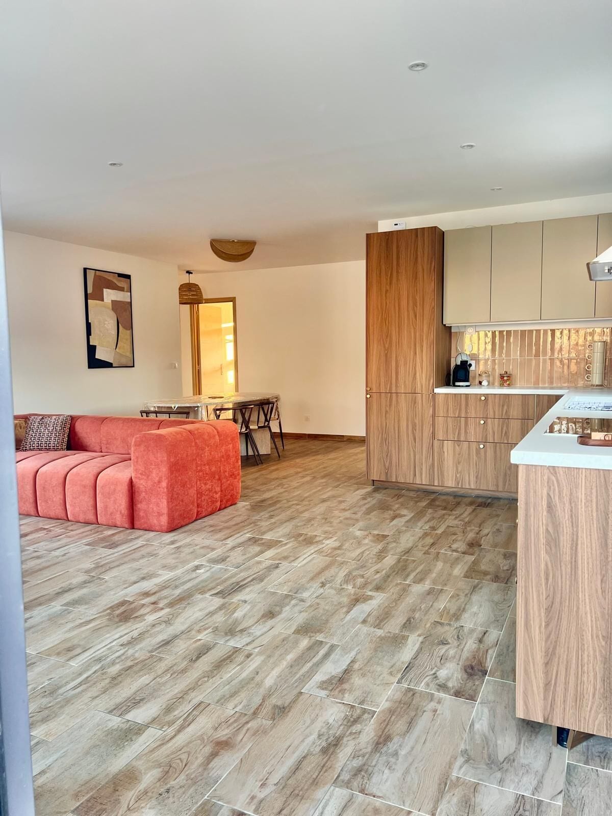 Ein modernes Wohnzimmer mit einem roten Sofa, einem Essbereich mit Tisch und Stühlen sowie einer Küche mit Holzschränken und einer Arbeitsplatte.
