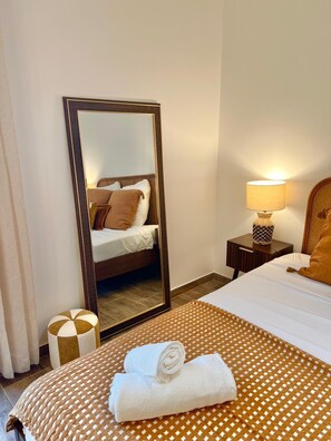 A hotel room with a bed, a nightstand with a lamp, a mirror, and a rolled towel on the bed. - June House in the Heart of the Luberon—Ducted Air Conditioning, All the Comforts, and a Private Garden (Saignon)