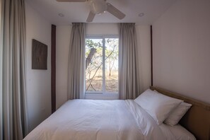 Une chambre à coucher avec un lit, un ventilateur de plafond et une fenêtre avec des rideaux.
