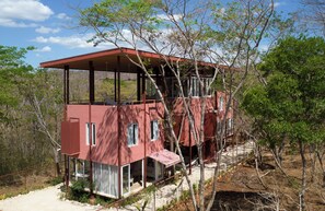 Un bâtiment rouge à deux  étages, doté d’un patio couvert et entouré d’arbres.