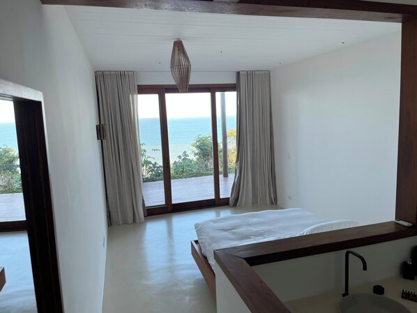 Un dormitorio con cama, ventana con cortinas y vista al mar.