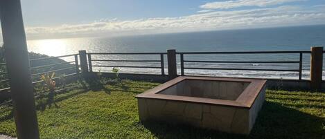 A patio area with a wooden deck, a stone planter, and a view of the ocean.