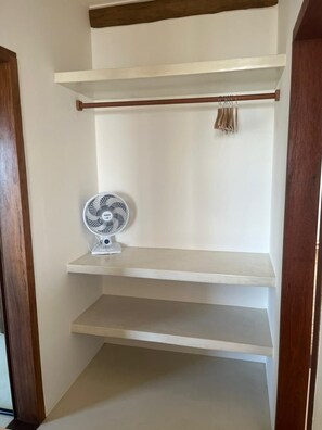Una habitación con un ventilador blanco en el suelo, un marco de puerta de madera y una pared blanca con un estante.