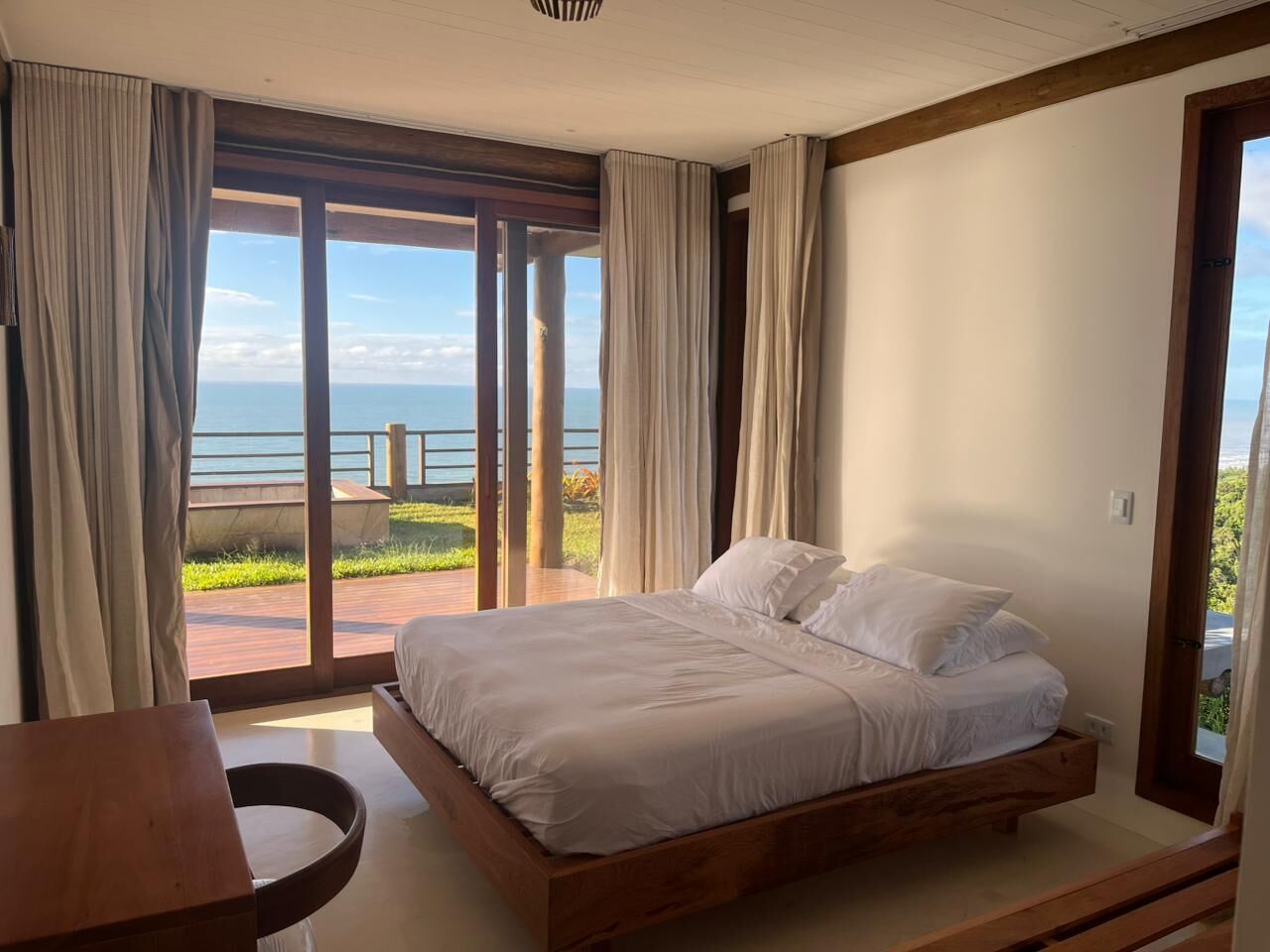 Ein Schlafzimmer mit einem großen Bett, einem Holzkopfende und Meerblick durch raumhohe Fenster.