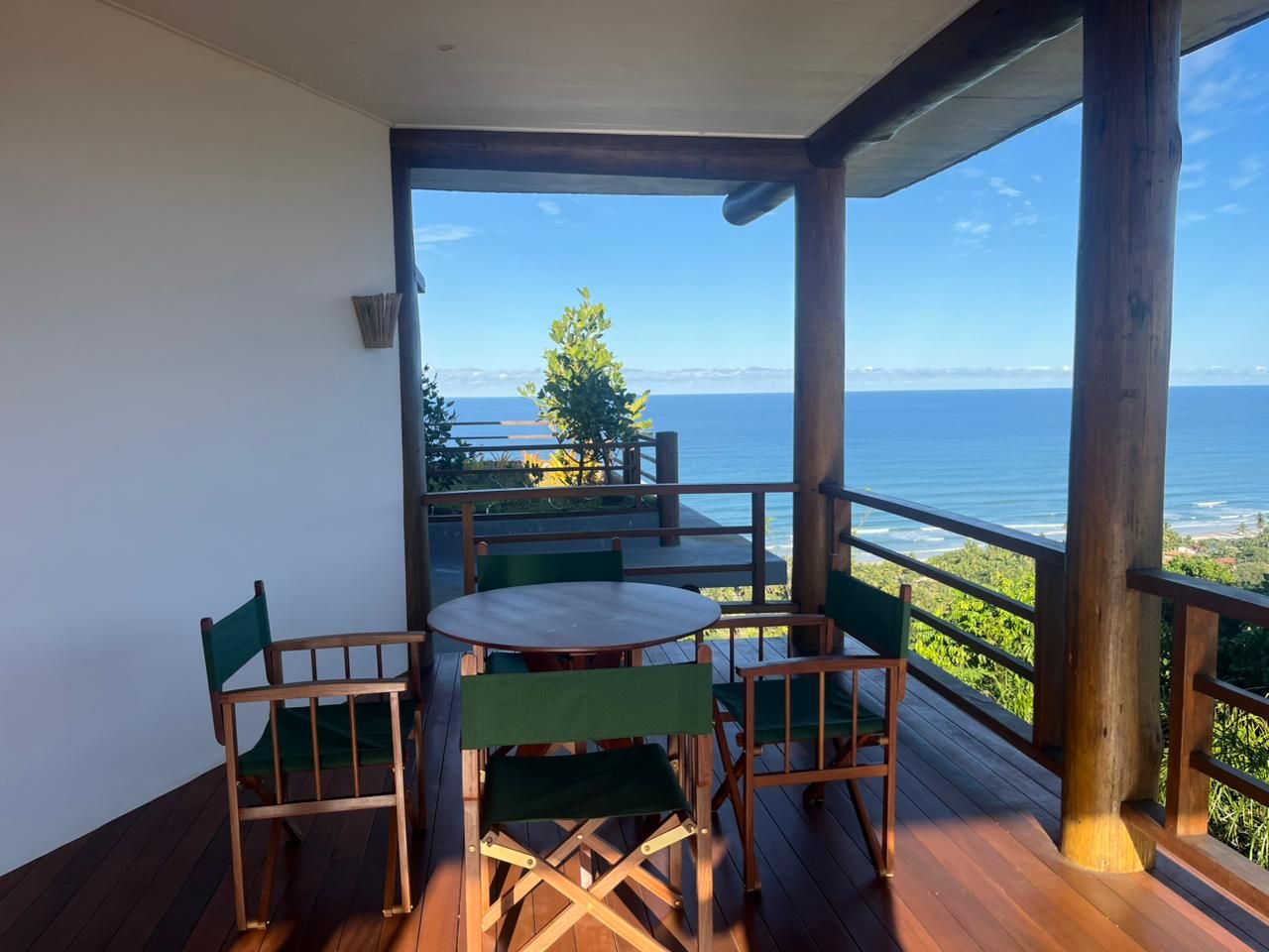 A wooden deck with a table and chairs, overlooking a scenic view of the sea and greenery.