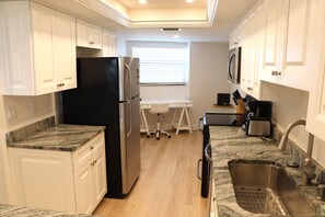 A compact kitchen with white cabinetry, a black refrigerator, a countertop with a sink, and a window with blinds. - Gulf and bay Club - C310 (Siesta Key)