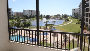 Un balcon avec vue sur une piscine, une fontaine et un espace paysager agrémenté de palmiers.