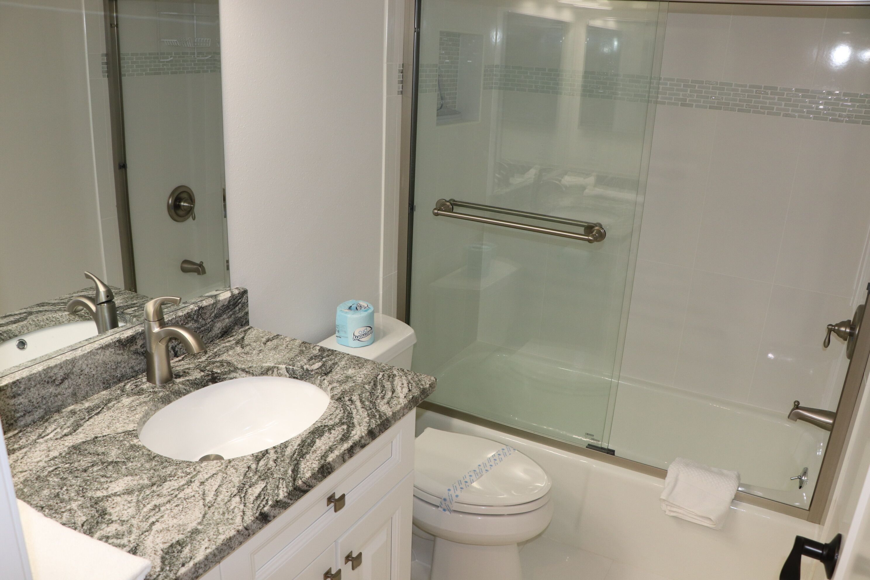 A bathroom with a granite countertop sink, a mirror, a toilet, and a glass-enclosed shower area.