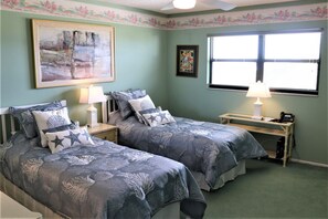 Un dormitorio con dos camas, un escritorio, una silla, una lámpara y un cuadro en la pared.