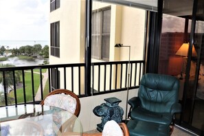 A balcony with a view of a body of water, a table with chairs, and a lamp. - Gulf and Bay Club - D506 (Siesta Key)