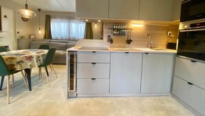 A modern kitchen with a central island, built-in appliances, and a dining area with a table and chairs. - Chalet in a 5-star resort with swimming pools (Puget-sur-Argens)