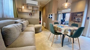 A modern living room with a sofa, dining table, chairs, and built-in shelving. - Chalet in a 5-star resort with swimming pools (Puget-sur-Argens)