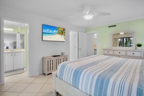 Ein Schlafzimmer mit einem Bett, einem Schminktisch, einem Fernseher, der eine Strandansicht zeigt und einem Kleiderschrank.