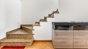 A staircase with a granite finish, leading to a kitchen area with a dark countertop and wooden cabinets. - GuestHost - Sweet Home in Portoscuso! (Portoscuso)