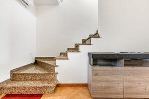 A staircase with a granite finish, leading to a kitchen area with a dark countertop and wooden cabinets. - GuestHost - Sweet Home in Portoscuso! (Portoscuso)