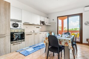 A modern kitchen with built-in appliances, a dining area with a table set for four, and a sliding glass door leading to an outdoor patio.