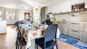 A modern kitchen with white cabinets, a microwave, and a sink. There is a dining area with a table set for four, chairs, and a blue rug. - GuestHost - Sweet Home in Portoscuso! (Portoscuso)