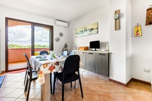 A dining area with a table set for four, a kitchen area with a refrigerator and a microwave, and a sliding glass door leading to a balcony.
