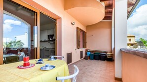 A balcony with a table set for two, a kitchen area, and a view of the surrounding neighborhood. - GuestHost - Sweet Home in Portoscuso! (Portoscuso)