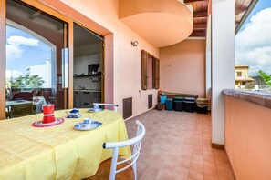 A balcony with a table set for two, a kitchen area, and a view of the surrounding neighborhood. - GuestHost - Sweet Home in Portoscuso! (Portoscuso)