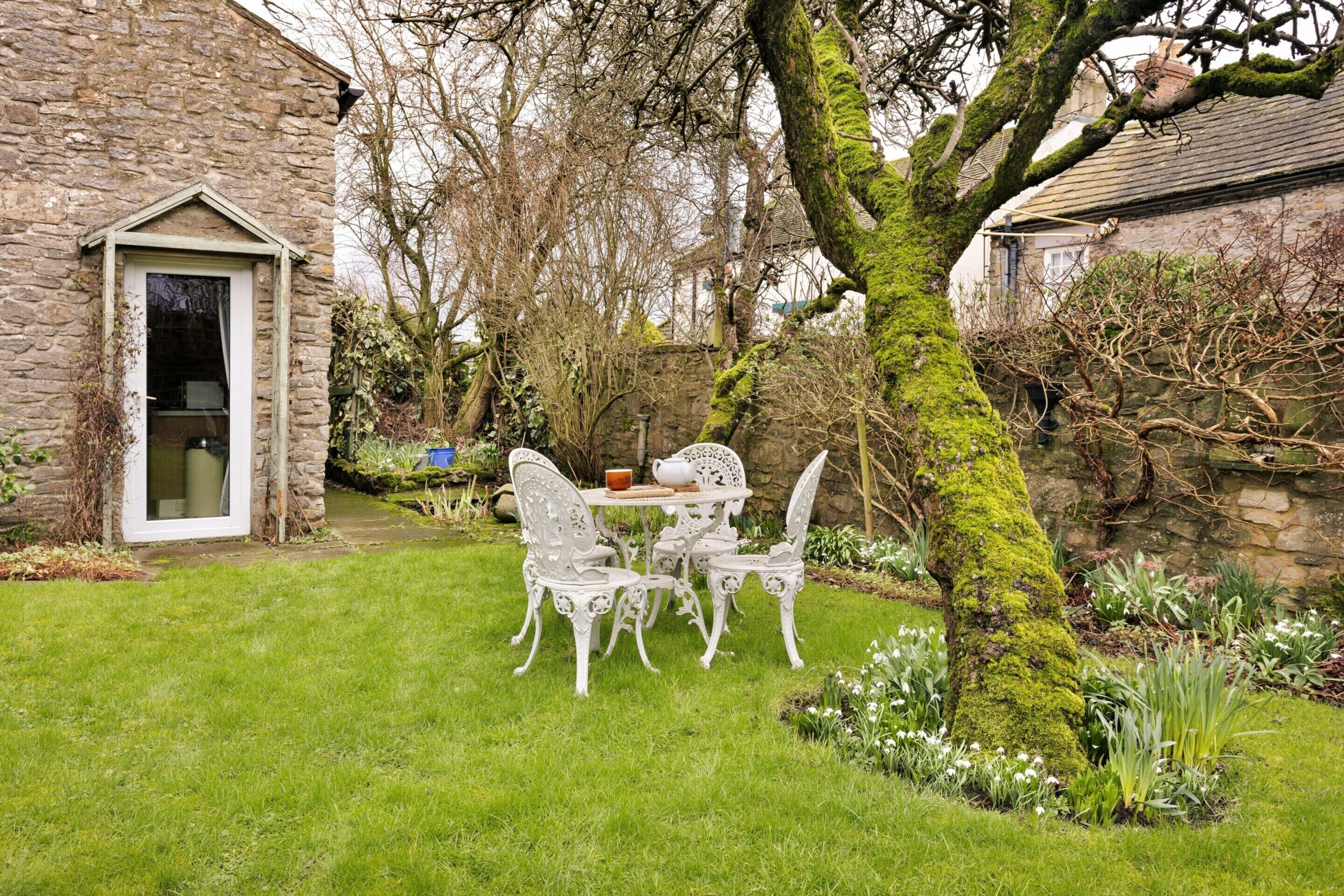 Een stenen gebouw met een deur en een kleine tuin met een tafel en stoelen.