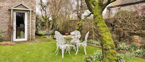 Een stenen gebouw met een deur en een kleine tuin met een tafel en stoelen.