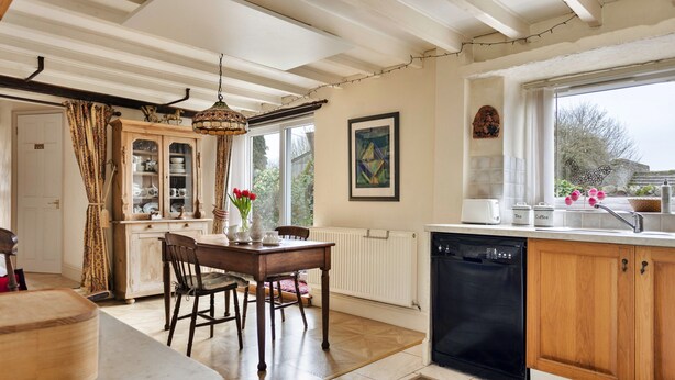 A kitchen with wooden cabinets, a dining table, chairs, a radiator, and a dishwasher. - Grand Devon Country House for 15 (Leyburn)
