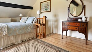 A bedroom with a bed, bedside lamps, a dresser with a mirror, and a painting on the wall. - Grand Devon Country House for 15 (Leyburn)