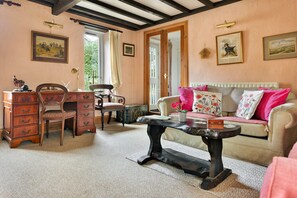 A cozy room with a wooden desk, a chair, a sofa with floral cushions, and a large window. - Grand Devon Country House for 15 (Leyburn)