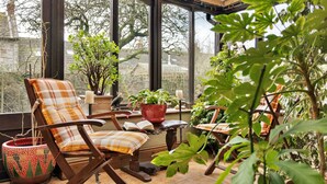 A cozy reading nook with a wooden chair, a small table, and a variety of potted plants. - Grand Devon Country House for 15 (Leyburn)