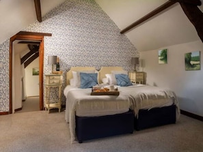 A bedroom with a sloped ceiling, a bed with a headboard, bedside tables, and artwork on the walls. - Georgian Devon House With Hot Tub (Ilfracombe)
