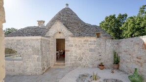 A stone building with a conical roof, a doorway, and a small patio area with plants and a green bottle. - A charming trulli complex wit pool and 2000sqm of land planted with olive trees; it hosts 6 guests with 3 independent sleeping areas and 3 bathrooms. Located just 3 km from Alberobello and midway between the Adriatic and Ionian coasts, in the countryside (Martina Franca)