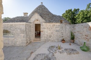 Ein Steinhaus mit einem Kegeldach, einem Eingang und einer kleinen Terrasse mit Pflanzen und einer grünen Flasche.